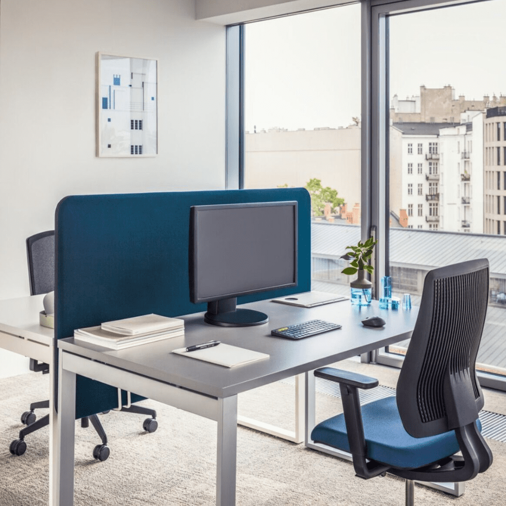 biurka pojedyncze przedzielone dużą niebieską ścianką tapicerowaną mocowaną do blatów biurek szary metalowy stelaż biurek połączony z blatem antracytowym fotele biurowe obrotowe z siedziskiem niebieskim i oprciem z siatką OGI Q