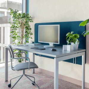 biurko na białych nogach stalowych z szarym blatem i niebieską ścianką tapicerowaną przed biurkiem szare designerskie krzesło na kółkach